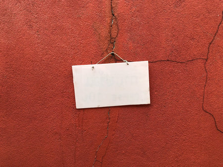 Empty white board hanging on an orange wall.の素材