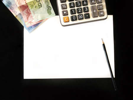 Top view of calculator pen pencil and money on black table.の素材