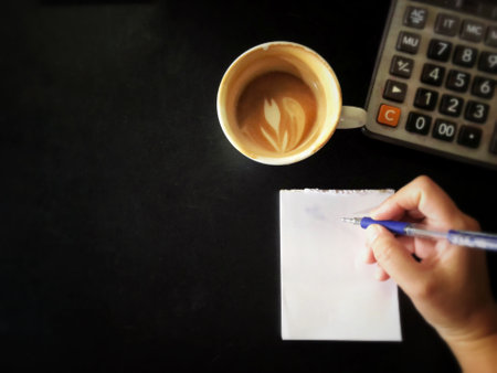 Close up image of a woman writing on a paper with a pen and a cup of coffeeの写真素材