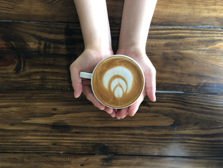 A cup of latte art coffee in woman hand on wooden backgroundの写真素材