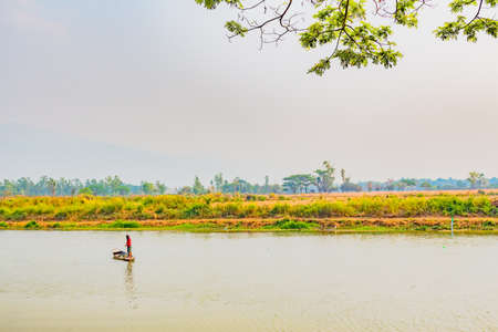The fisherman in the boat use net to catch fish in the river.の写真素材