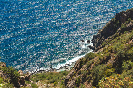 The view down from the mountain covered with green plants, to the rocky seaside and tourist tents in the distanceの写真素材