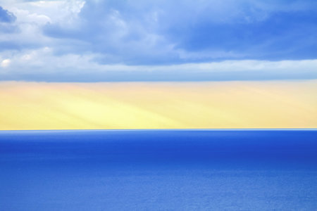 Pure sea landscape, in the upper third of blue clouds, down the middle a band of pure yellow sky at sunset, a band of blue calm sea in the lower third of the frameの写真素材