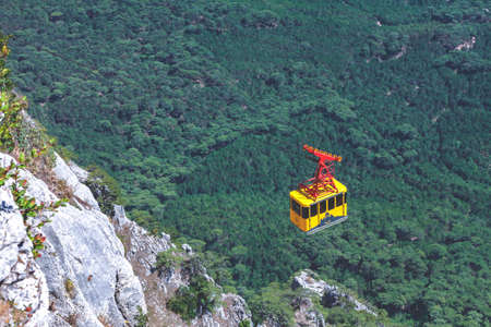 Ai-Petri, Crimea, August 2020: the yellow cable car rises above the rocky mountains and green forestの写真素材