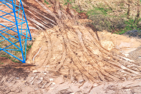 Bulldozer tracks on wet ground with puddles next to blue metal tower