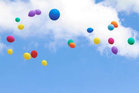 Many colorful balloons fly up into the blue sky with white cloudsの写真素材