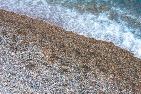 Pebbled gray beach and sea surf with white foamの写真素材