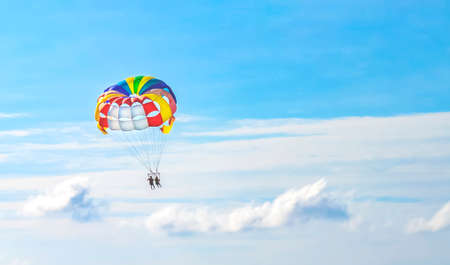 Two people flying in the bluecloudy sky on a multi-colored parachute.の写真素材