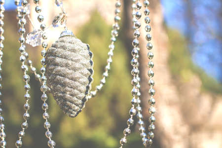 Festive decoration, shiny, silvery, gray Christmas tree toy pine cone with silver beads hang on a natural background in haze close upの写真素材