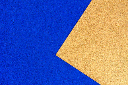 Shiny textured rich blue and gold glitter paper background, gold sheet of paper lies in the corner on blueの写真素材