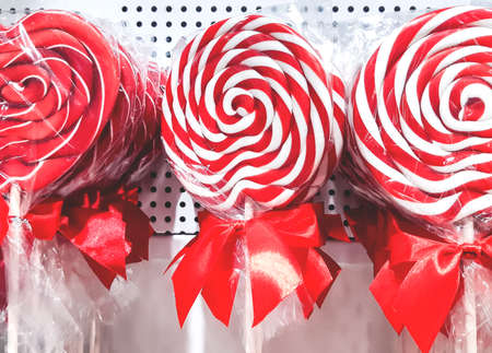Close-up of bright colorful striped red and white lollipops in transparent packaging and red bows on a shop windowの写真素材