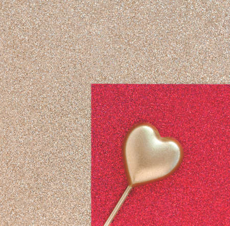 Gold heart on a stick on the right against the background of paper with glitterの写真素材