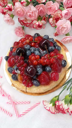 Berry birthday cake. Cheesecake with cherries, raspberries, currants and blueberries. Cake, pink candles and red flowers on a white background. Photo for stories.の写真素材