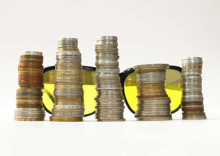Sunglasses, background, stakes of diverse coins foreground, on whiteの写真素材