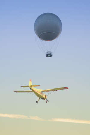 Helium balloon and a yellow aircraft seen against colorful sky at dusk, jest-trail visible in the backgroundの写真素材
