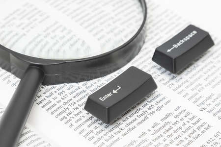 Enter and Backspace Computer Keys and a magnifying glass placed on a book pageの写真素材