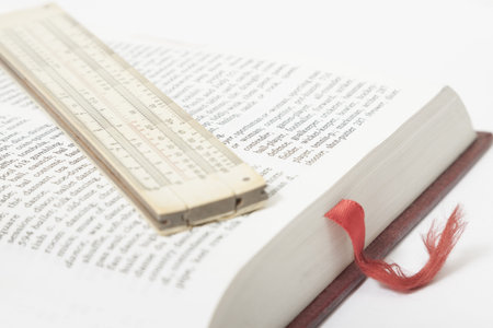 Vintage slide rule placed on a book page, red bookmark visible