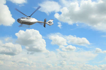 Silver helicopter in mid-air against overcast sky, white clouds in the backgroundの写真素材