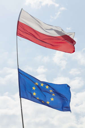 Flags of Poland and EU flying on the same flagpole, sunlit, sky in the backgroundの写真素材