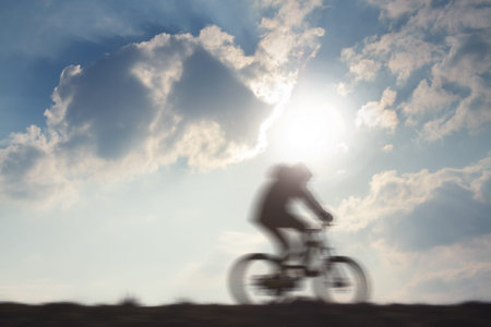Cyclist in motion against sun and overcast sky, motion blur