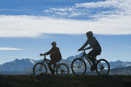 Silhouette of two cyclists against mountain landscape and overcast skyの写真素材