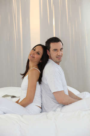 Couple sitting back to back on a bedの写真素材