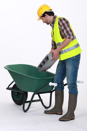 Worker putting a concrete block into a wheelbarrow