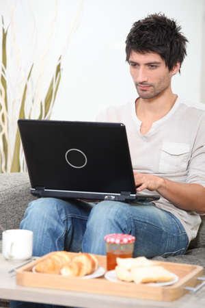 Man having breakfast whilst using laptopの写真素材