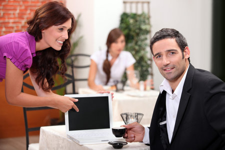 Woman in a restaurant pointing to a computer screen left blank for your image