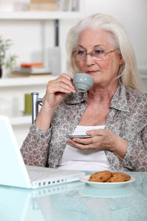 Elderly lady drinking coffee and using laptopの写真素材