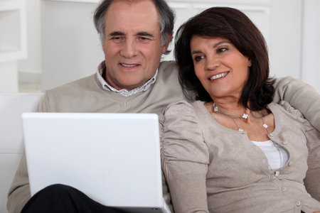 Middle-aged couple with laptop sat on sofaの写真素材