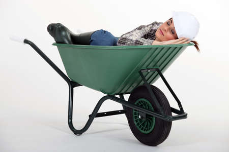 A female construction worker sleeping in a wheelbarrow.の写真素材