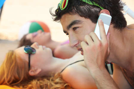 young man phoning at the beach with his friendsの写真素材