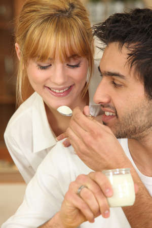 Man feeding a spoonful of yoghurt to his girlfriendの写真素材