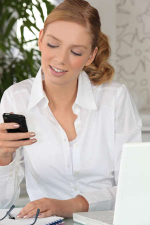 Young woman checking her cellphone at her deskの写真素材