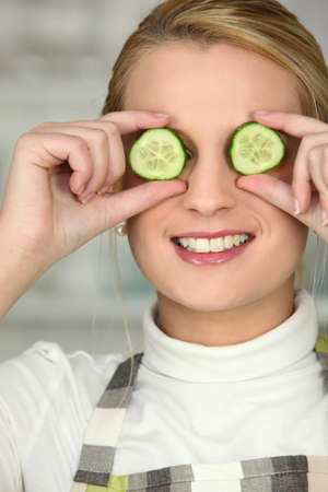 blonde wearing apron hiding eyes with cucumber slicesの写真素材
