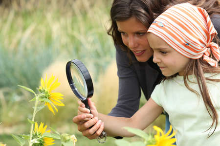 Mother and daughter looking at a flower with a magnifying glassの写真素材