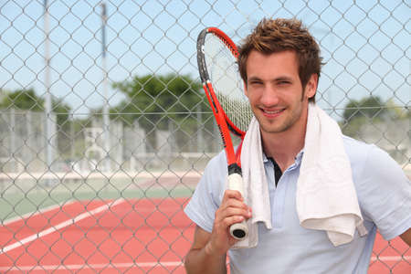 A tennis player posing in front of a tennis court with his racket. A tennis player posing in front of a tennis court with his racket.