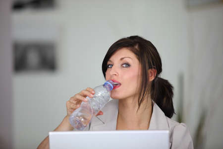 portrait of classy brunette working on laptop with bottle of waterの写真素材