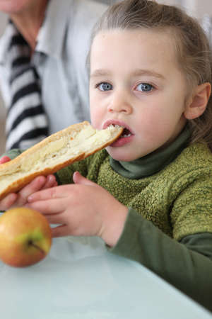 Girl eating slice of buttered breadの写真素材