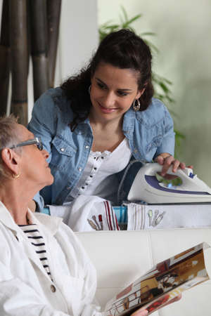 a young woman ironing and talking to an older womanの写真素材