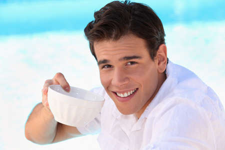 Handsome young man drinking from a bowlの写真素材