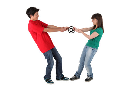 Teenagers pulling from each side of an at sign, studio shot