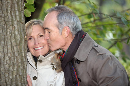 Older man kissing his partner under a tree