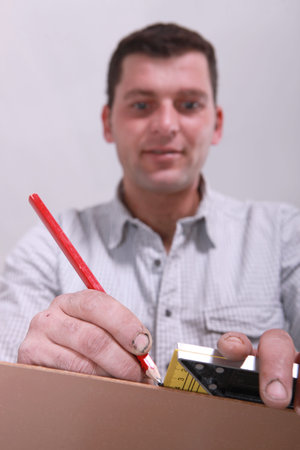 Closeup of a man measuring a piece of wood and marking it with a pencil