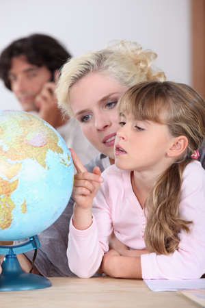 a mother is showing to her daughter some country on a globe, her husband is on the phoneの写真素材