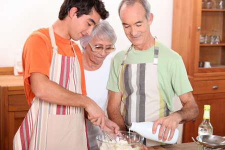a 20 years old boy and 65 years old man and woman making cake togetherの写真素材