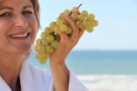 Woman eating a bunch of grapes by the seaの写真素材