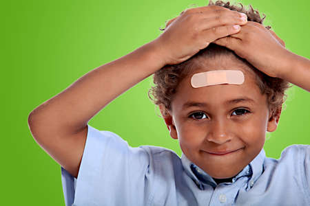 coloured little boy with plaster on his forehead against fluorescent green backgroundの写真素材