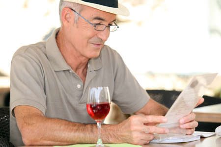 elderly gentleman seated in cafe drinking glass of red wineの写真素材